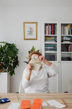 Adult woman conceals face with banknotes in a modern indoor office space.