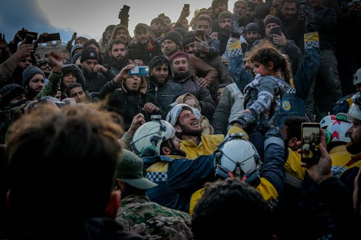 Rescue workers celebrate saving a child in Idlib, Syria amid a supportive crowd.