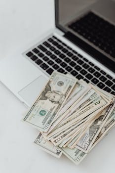 Stack of US dollar bills on a laptop keyboard representing online finance and budgeting.