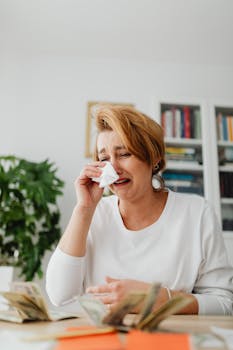 Woman crying over financial problems, surrounded by money indoors.