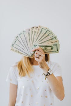 Woman holding a fan of US dollar bills in front of her face.