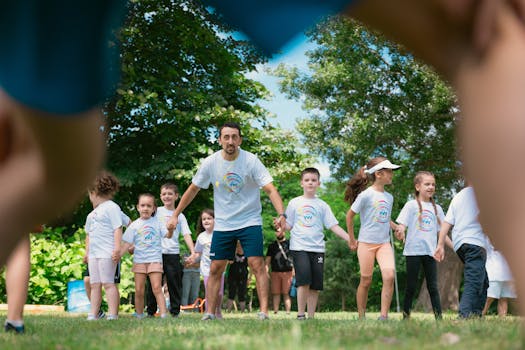 Children and an instructor playing together in a sunny park, holding hands and enjoying outdoor activities.