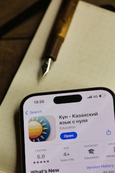 Mobile app for learning Kazakh language featured on a smartphone next to a fountain pen.