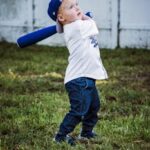 A child with a blue cap and bat prepares to swing in a grassy area.