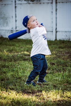 A child with a blue cap and bat prepares to swing in a grassy area.