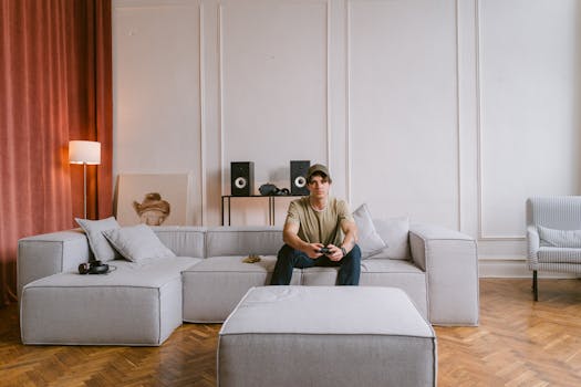 A young man sits on a modern sofa playing video games in a stylish living room interior.