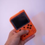 Close-up of a retro orange gaming console held in a hand, showcasing buttons and screen.