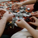 Close-up of multiple hands working together to solve a puzzle on a table indoors.