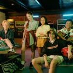 Diverse group of teens having fun in a vintage arcade with retro games and vibrant neon lights.