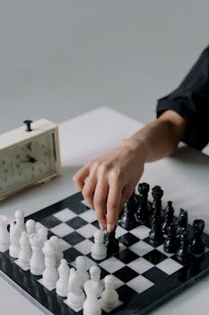 Hand moving chess piece on board next to a chess clock. Perfect for strategy and game concepts.