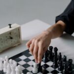 Hand moving chess piece on board next to a chess clock. Perfect for strategy and game concepts.