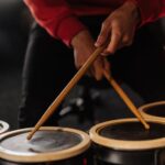 Hands holding drumsticks playing drums indoors, capturing musical performance.