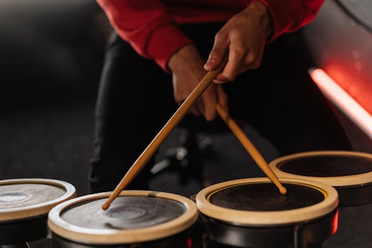 Hands holding drumsticks playing drums indoors, capturing musical performance.