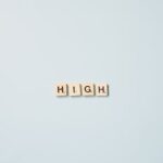 Minimalist art featuring Scrabble tiles spelling 'HIGH' on a light blue background.