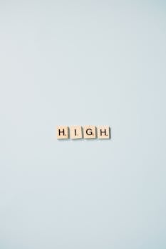 Minimalist art featuring Scrabble tiles spelling 'HIGH' on a light blue background.