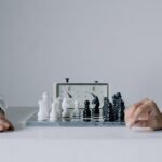 Two players engaged in a focused chess match with chess clock on table.