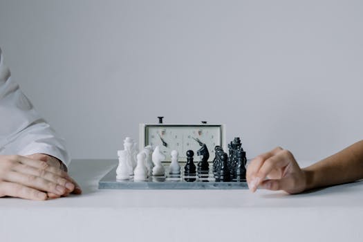 Two players engaged in a focused chess match with chess clock on table.