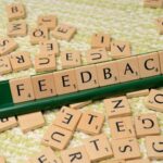 Wooden letter tiles spelling 'feedback' on a green rack, representing communication and evaluation.